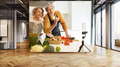 Happy aged caucasian couple famous bloggers cooking healthy dinner and streaming on cellphone in kitchen interior Wall mural