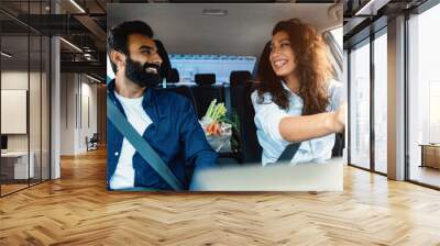 Happy arab couple driving home after shopping in supermarket, bag full of fresh vegetables on the back seat of car Wall mural