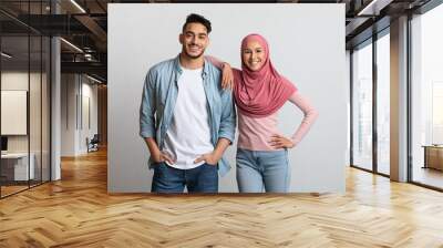 Happy arab man and young woman in hijab posing over gray background Wall mural