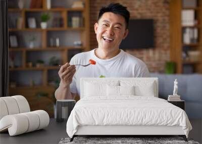 Happy asian mature man holding fork and bowl with fresh vegetable salad, eating healthy lunch after domestic training Wall mural