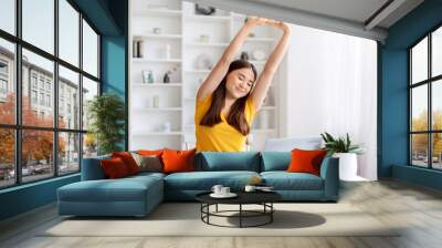 Happy asian woman stretching with her arms raised, taking break at her home office Wall mural