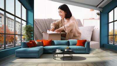 Happy asian woman unpacking parcel after online shopping Wall mural