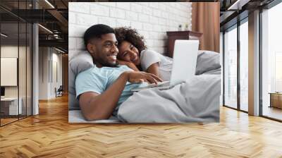 Happy black couple in bed with laptop at home Wall mural