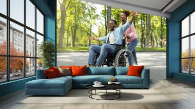 Happy black disabled guy in wheelchair on walk with his loving girlfriend outdoors, having fun, spending time together Wall mural