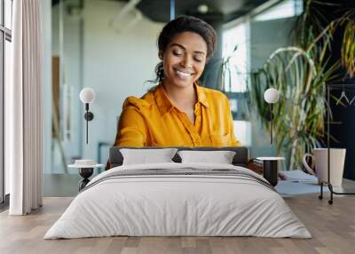 Happy black female company worker working with documents, writing and doing paperwork, sitting at workplace in office Wall mural