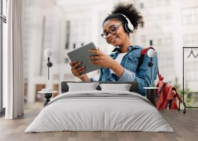 Happy Black Female Student Using Tablet Computer Wearing Headphones Outside Wall mural