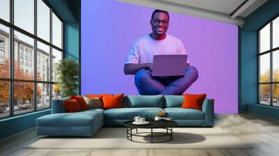 Happy Black Student Guy In Eyeglasses Sitting With Laptop In Neon Lighting Wall mural