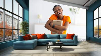 Happy black woman hugging cardboard parcel, receiving desired product, getting online order delivered at home Wall mural