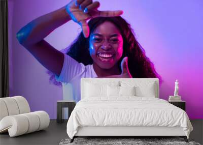 Happy black woman making picture frame with fingers, looking at camera and smiling for photo in neon light Wall mural