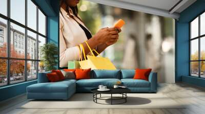 Happy black woman using smartphone, holding shopping bags Wall mural