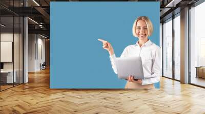 Happy business lady with laptop computer pointing aside at space for your text, blue studio background Wall mural