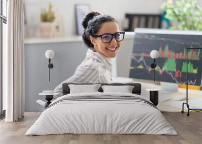 Happy businesswoman sitting at workplace in office and smiling at camera, computer monitor with graph on background Wall mural