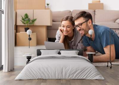 Happy couple searching online with a laptop over a cardboard box Wall mural