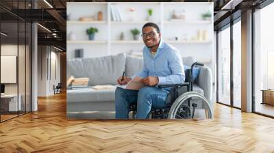 Happy disabled black guy in wheelchair taking notes, looking at camera and smiling at home, copy space Wall mural