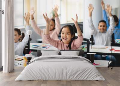 Happy diverse small schoolchildren raising hands at classroom Wall mural