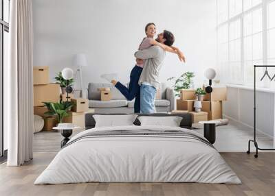 Happy excited european millennial husband raises wife have fun in living room interior with cardboard boxes Wall mural