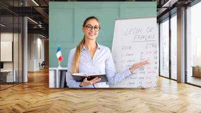 Happy French teacher explaining foreign language rules near blackboard indoors and smiling at camera Wall mural