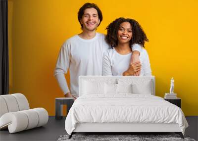 Happy interracial couple cuddling while posing over yellow background Wall mural