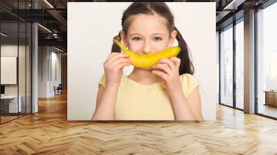 Happy little girl having fun with banana over white background Wall mural