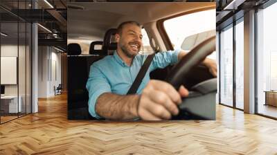 Happy man in earphones enjoying music driving luxury car Wall mural