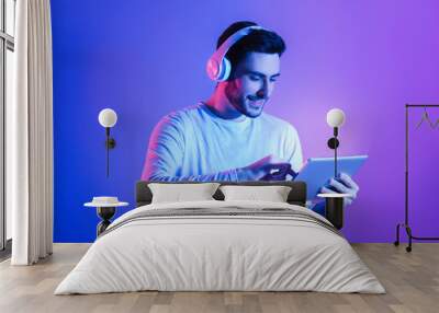 Happy man in wireless headphones uses tablet Wall mural