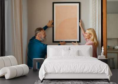 Happy Mature Couple Hanging Picture In Frame On Wall Indoors Wall mural