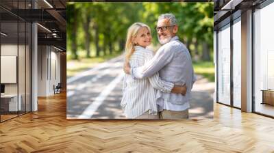 Happy mature spouses embracing while walking in summer park together Wall mural