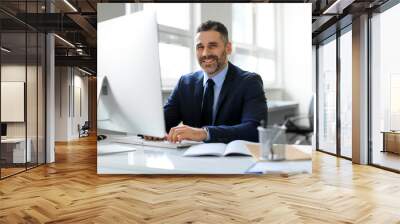 Happy middle aged businessman in suit sitting in office and smiling at camera, working with modern computer, free space Wall mural