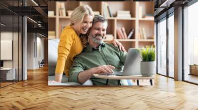 Happy middle aged couple websurfing on laptop together while relaxing at home Wall mural