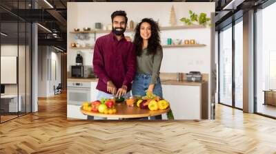 Happy middle eastern husband and wife cooking lunch in kitchen interior, looking at camera and smiling, copy space Wall mural