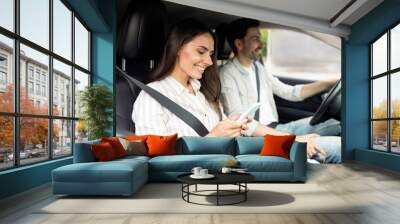 Happy millennial couple sitting inside white car, woman holding smartphone Wall mural