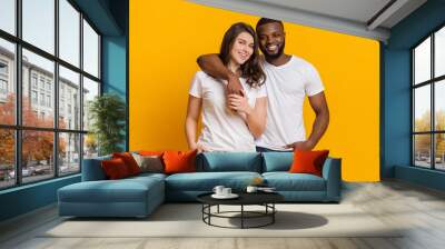 Happy multiracial couple hugging and posing over yellow background Wall mural