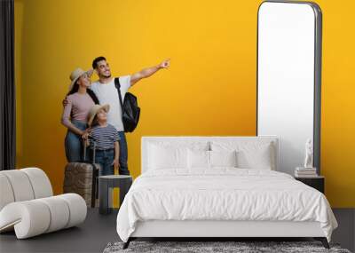 Happy parents with little daughter carrying suitcases, pointing at phone Wall mural