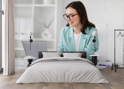 Happy pretty millennial european business lady in glasses uses computer to chat, enjoy work in white office Wall mural