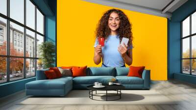 Happy shopper with credit card and phone on yellow Wall mural