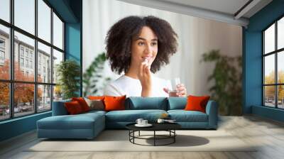 Happy smiling young african american woman taking pill or vitamin with cod liver oil omega-3 Wall mural