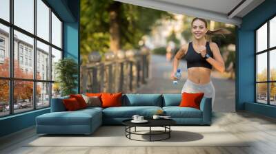 Happy sporty millennial woman running on quay Wall mural