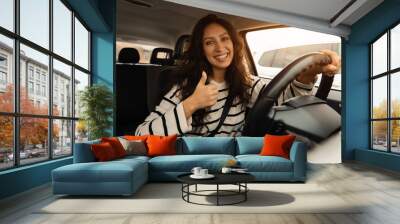 Happy woman sitting in car showing thumbs up gesture Wall mural