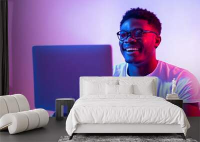 Happy young black man using laptop computer for online work, education or communication in neon light Wall mural