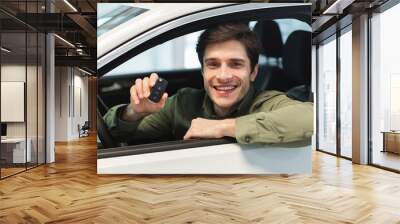 Happy young Caucasian man showing key from auto, sitting inside car salon, buying brand new automobile at dealership Wall mural