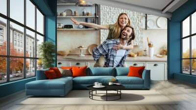 Happy young european guy rolls his wife on back and have fun together in modern kitchen interior in own home Wall mural