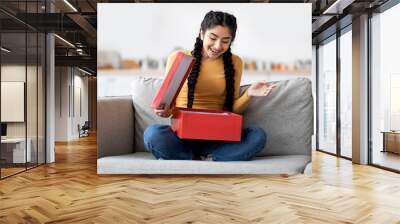 Happy young indian woman opening delivery box at home and looking inside Wall mural