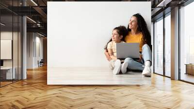 Happy Young Mother And Little Daughter Sitting With Laptop On Floor Wall mural