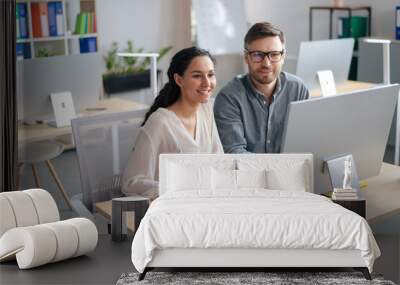 Happy young woman and her male colleague working together, using modern computer in open space office Wall mural