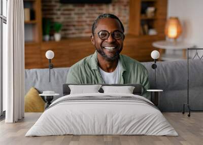 Headshot of cheerful adult african american man in glasses and casual relaxing on sofa Wall mural