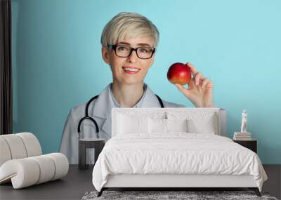 Healthy eating concept. Adult woman doctor in glasses holds red apple in hand Wall mural