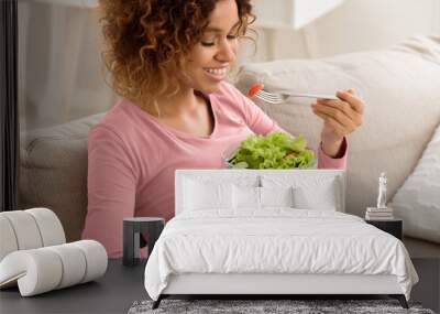 Healthy pregnancy food. African-american girl eating fresh vegetable salad, resting on sofa at home Wall mural