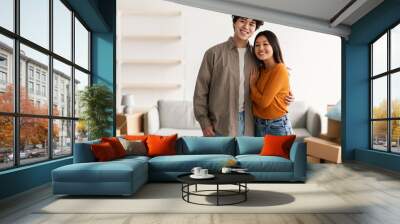 Home relocation concept. Joyful young Asian guy hugging his lovely wife in their new apartment, copy space Wall mural