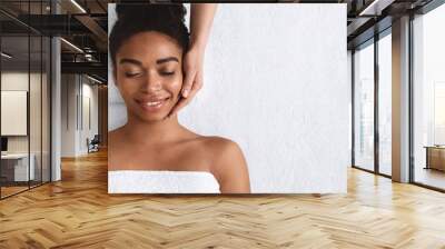 Joyful african girl having face massage at spa Wall mural