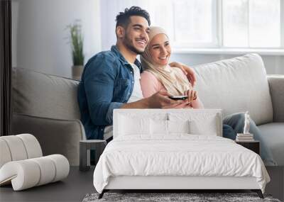 Joyful arab couple watching TV together at home Wall mural